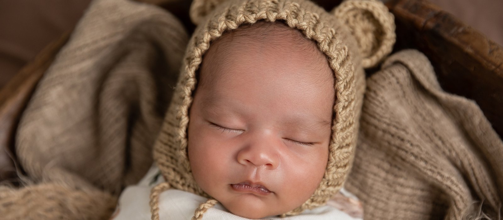 A sleeping newborn in a knitted bear bonnet
