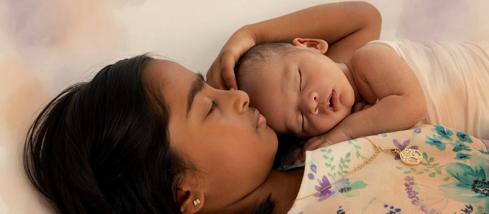 A young girl lying cheek to cheek with her sleeping newborn sibling