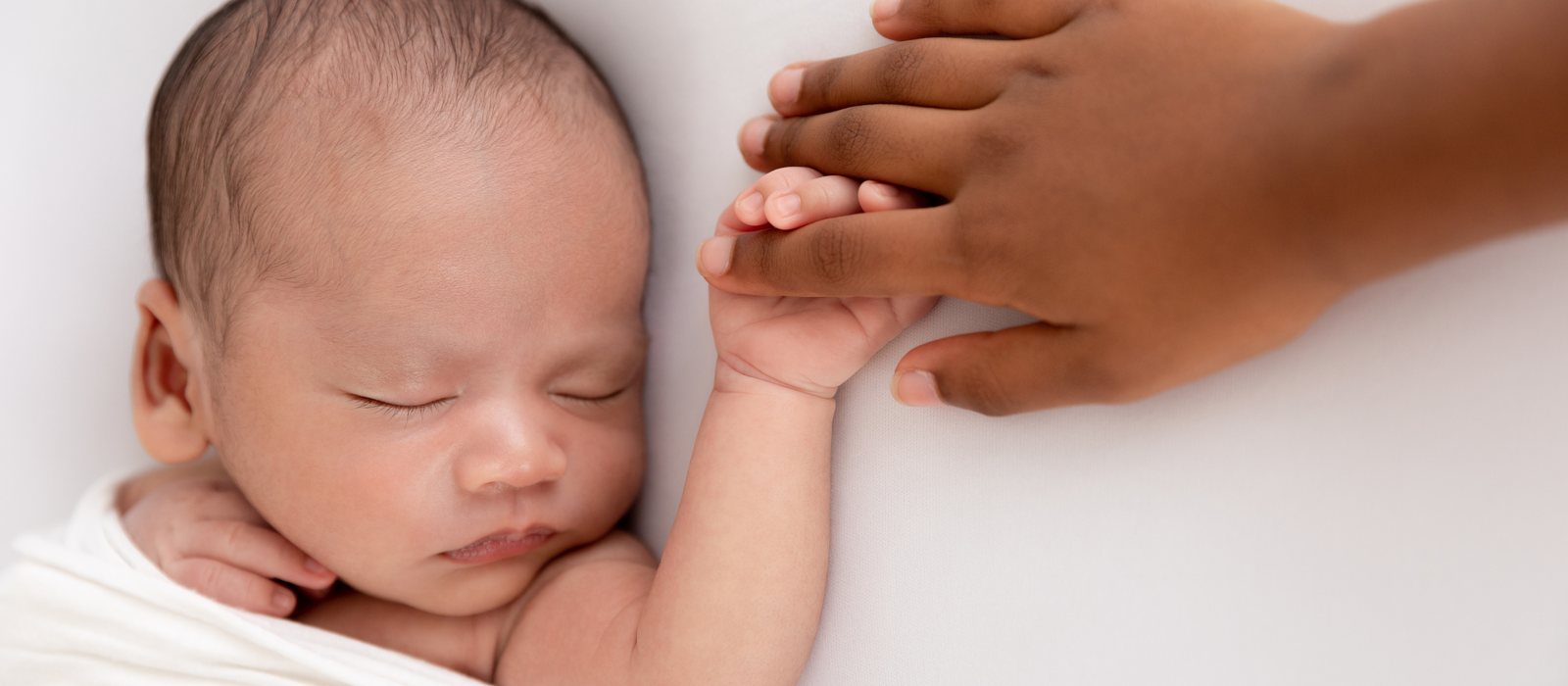 A newborn's hand grasping an adult's finger