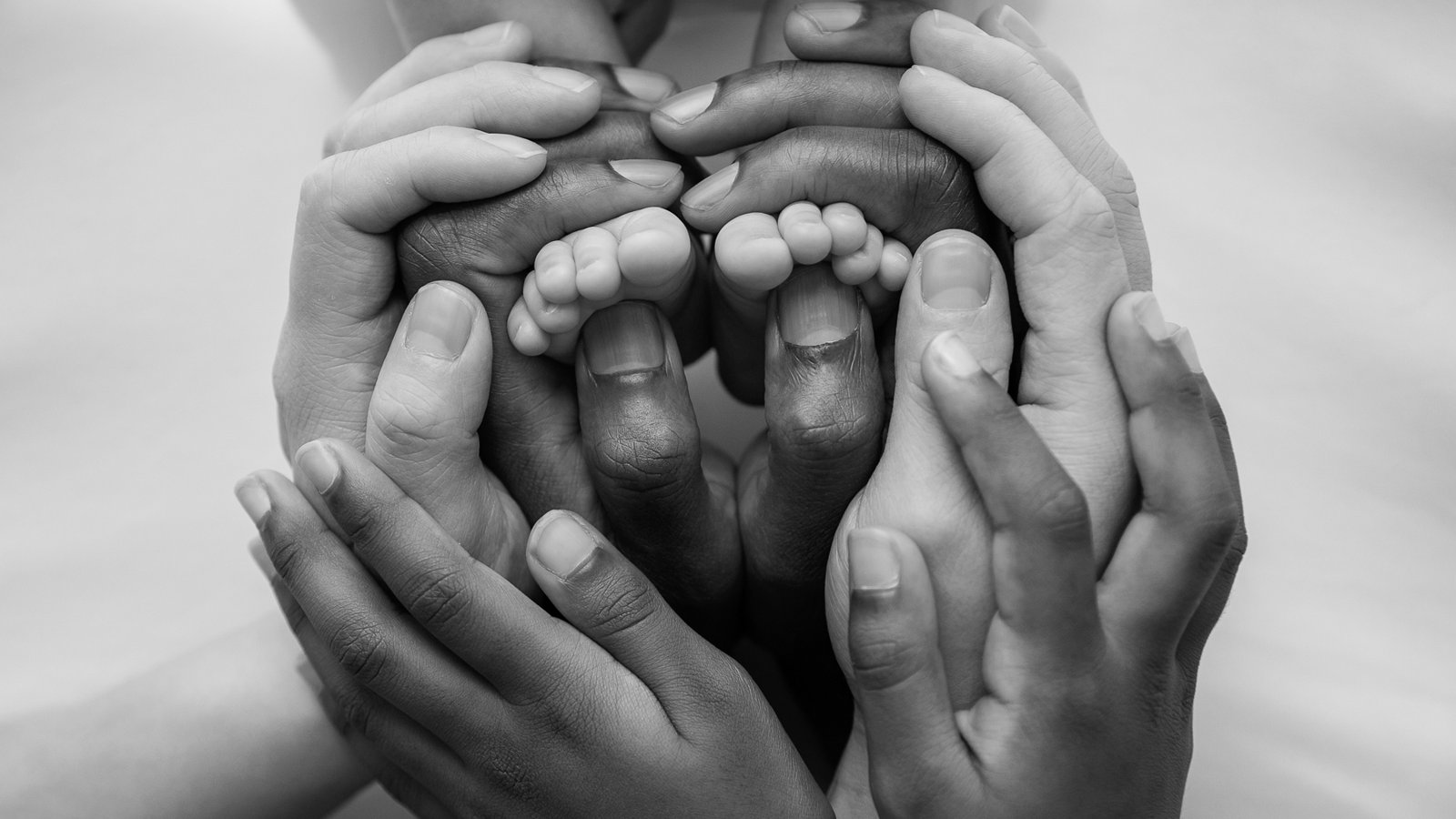 A family's hands gently cradling a newborn baby's feet